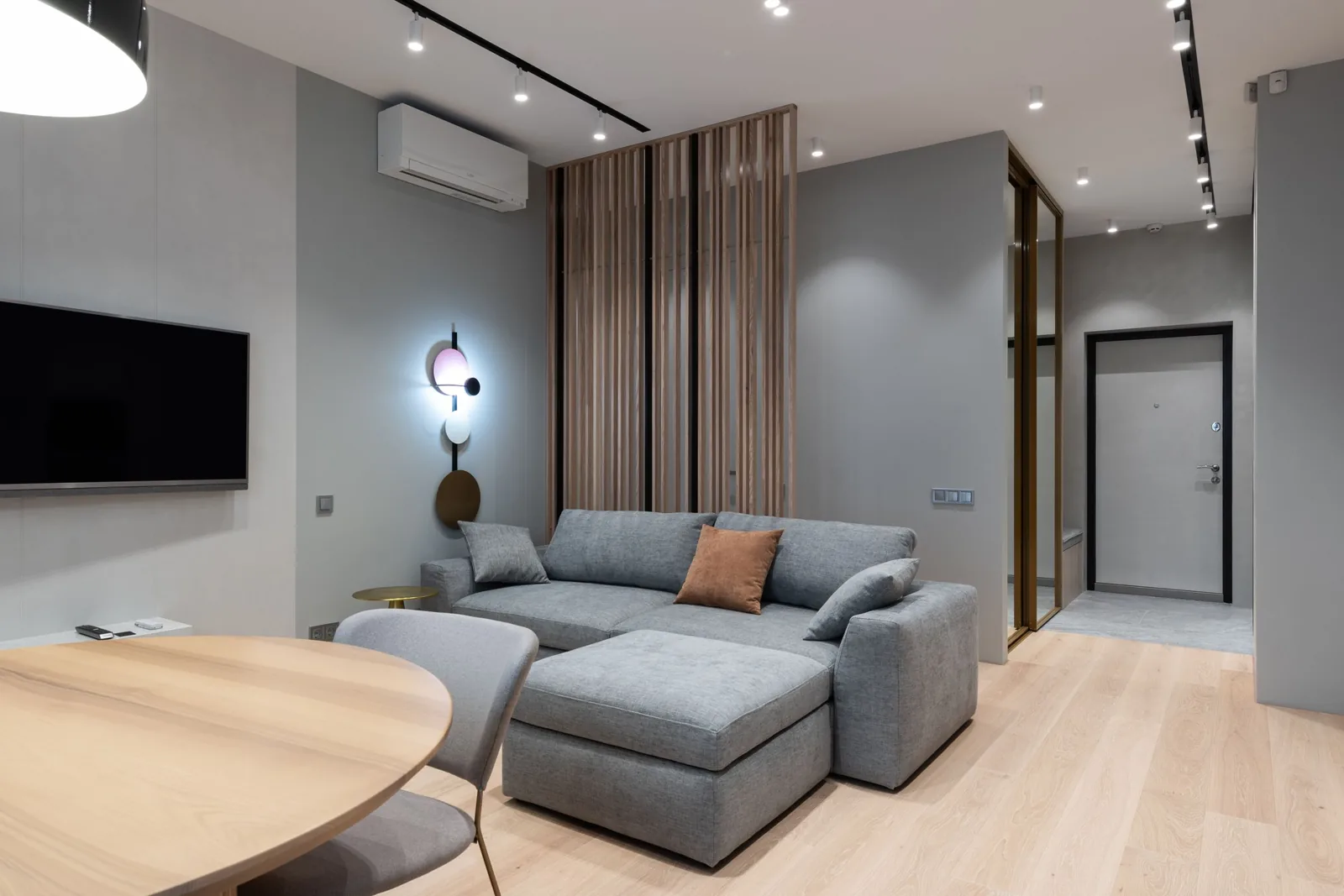 Nowoczesny salon z szarą kanapą narożną i drewnianym panelem ściennym